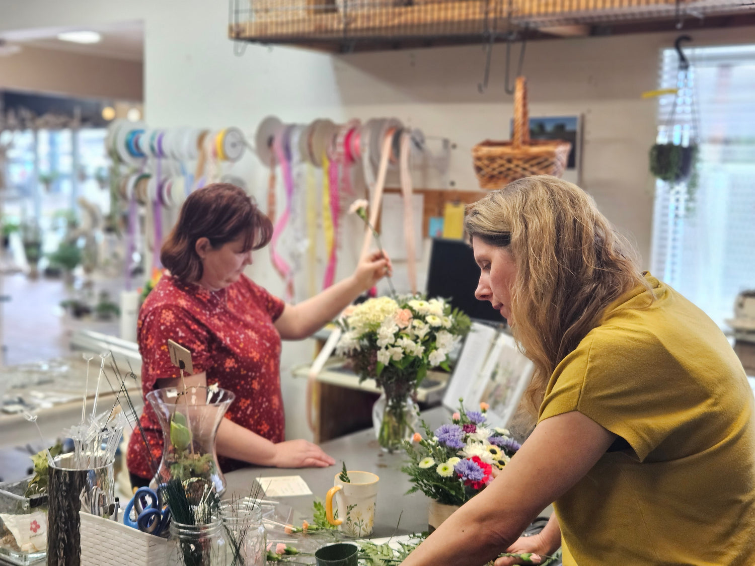 Two women working with flowers and ribbons in a workshop setting.