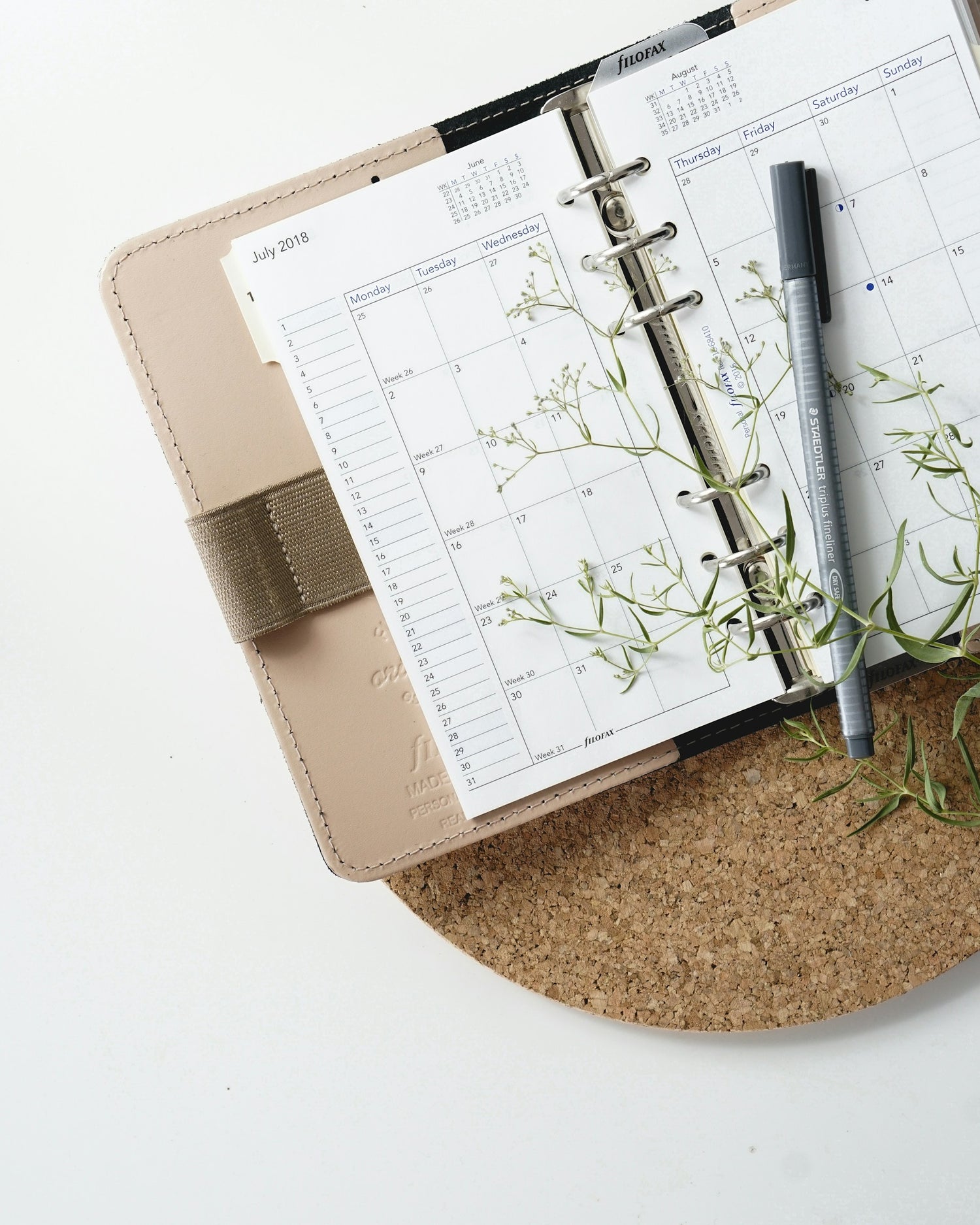 Planner with a pen and greenery on a cork coaster