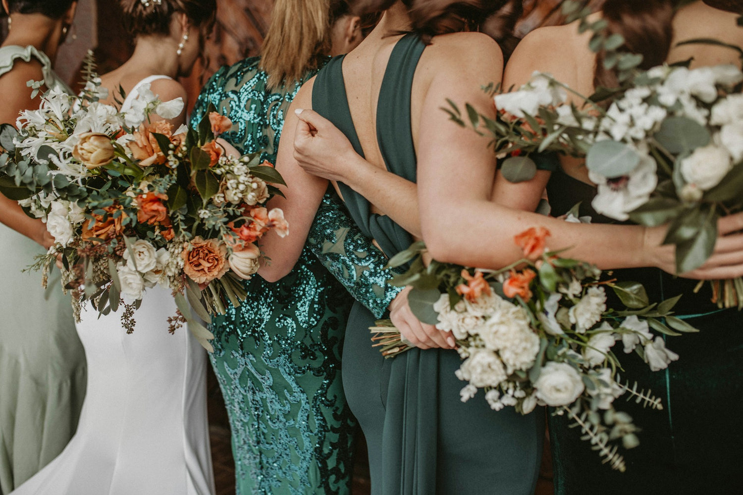 Bridesmaids in green dresses holding floral bouquets with a bride in a white dress.